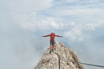 Climber finding his balance on top of a mountain ridge, surrounded by clouds, high on via ferrata...
