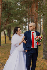 Happy bride and groom are standing in the autumn forest holding hands.