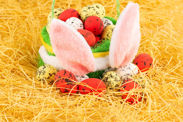Easter colorful eggs in basket and pink bunny ears on yellow straw background.