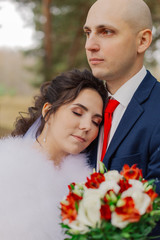 Happy bride and groom are standing in the autumn forest holding hands.