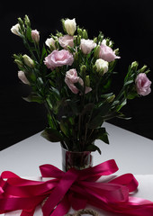 delicate bouquet of eustoma in a vase with silk ribbon on a dark background. Buds and flowers of...
