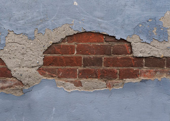 Close-up view of the old weathered exterior wall with peeling paint and plaster and a fragment of red brickwork underneath. Background with copy space in loft, grunge or industrial style