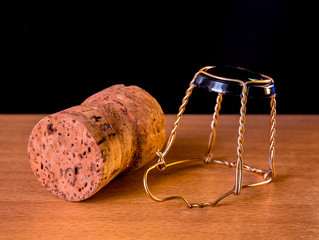 Cork plug with muselet(wire cage) from champagne or sparkling wine lies on a wooden surface with black background