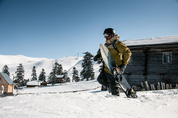 Male freerider walking on the the mountain snowcovered slope with a snowboard