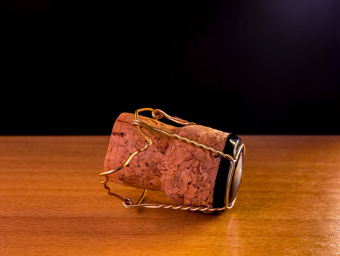 Cork plug with muselet(wire cage) from champagne or sparkling wine lies on a wooden surface with black background and a hint of lighting from the upper right corner