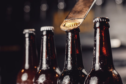 Glass ice cold bottles of beer with opener cap on dark background