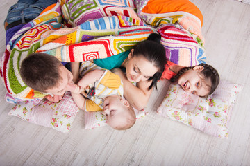 Happy family lie on the floor under colorfull blanket and laught. Indoor photo shot