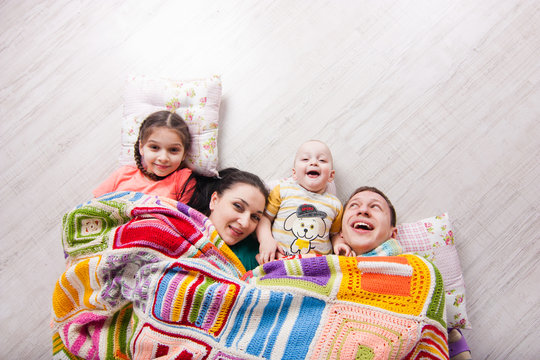 Happy family lie on the floor under colorfull blanket and laught. Indoor photo shot. Empty space for your text