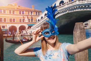 Portrait smiling young woman in Venice, Italy taking selfie while in Venetian mask against backdrop of great canal and bridge. Concept travel © Parilov