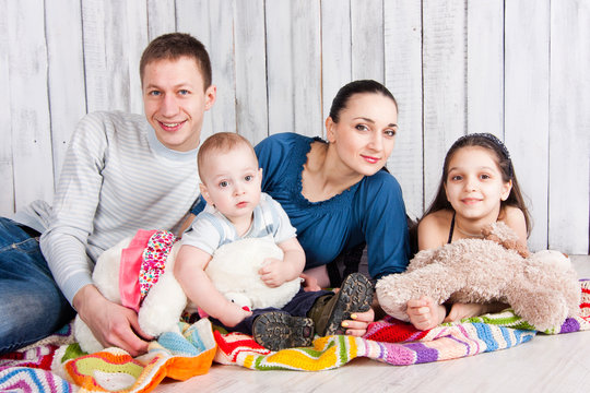 Happy smiling family lie with toys on colorful blanket on the floor and look on camera. Indoor photo shot