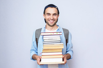 Happy student guy with a stack of books, portrait, gray background