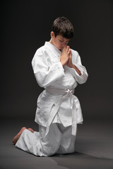 sport concept - greeting bow, a teenager dressed in martial arts clothing poses on a dark gray background, studio shoot