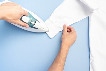 Concept of chores. Man ironing clean shirt, men's hands with iron, closeup, top view