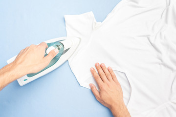 Concept of chores. Man ironing t-shirt, husband happy to do housework, top view, toned