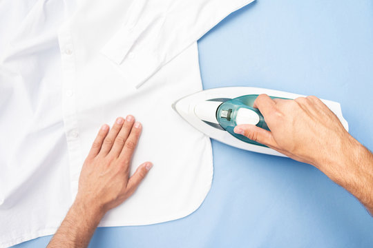 Concept of chores. Person ironing shirt, men's hands and iron, top view, cropped image