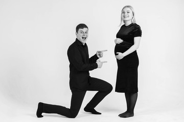 Pregnant woman and her husband smiling in black clothes on a white background. Black and white picture. Beautiful married couple. Copy, empty space for text