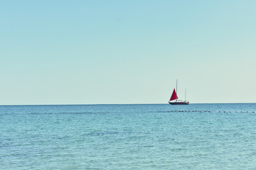 Red sailboat sailing on the sea, clear blue sky, copy space