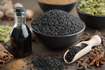 Black cumin or roman coriander seeds and black caraway oil bottles, aromatic spices on table:...