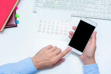 Man uses a smartphone, calendar on the desktop, top view, copy space