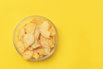 Crispy potato chips in glasses bowl on yellow background, top view