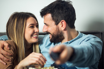 Smiling couple eating popcorn and using remote control