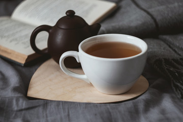 Cup of tean and teapot on wooden heart book and scarf on background