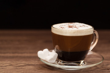 A Cup of coffee with milk on a wooden table and a heart-shaped marshmallow on a wooden table, on a dark background. Close up.