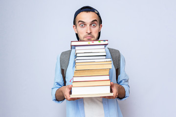 Funny student guy carries a heavy stack of books on gray background