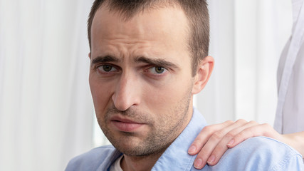 Concept of psychological assistance in the family. Portrait of a sad man, wife puts her hand on man's shoulder, close up, toned, 16:9