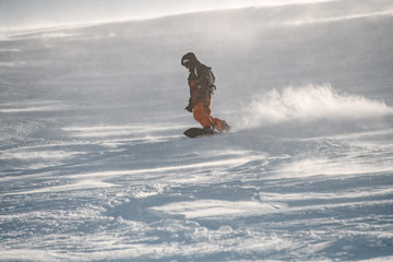 Freerider in a hood quickly descends from the top of the mountain on a snowboard