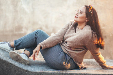 Plus zise model wearing sweater and glasses posing against street wall.