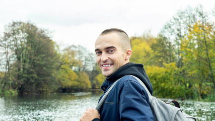 Young guy with a backpack smiling and looking at camera, man in the background of a beautiful landscape, rear view, toned, 16:9