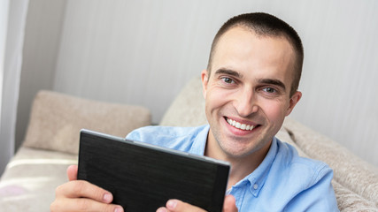 Handsome young man with e-book, man sitting on sofa at home, portrait, toned