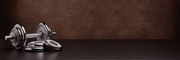 Obraz na płótnie Canvas Steel dumbbell and weights on brown background. Fitness, sport, healthy lifestyle concept. Extra wide panorama banner background