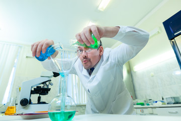 Chemist crazy. A mad scientist conducts experiments in a scientific laboratory. With a mad expression on his face, he mixes two liquids in a flask.