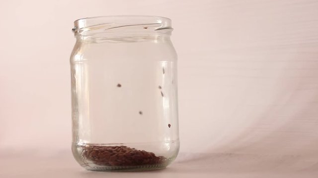 Flax seeds are poured into a jar from a paper bag, for cooking - pouring flax seeds from a paper bag into a glass jar to close opens a glass jar and pours flax seeds from a paper bag into it. in a gla