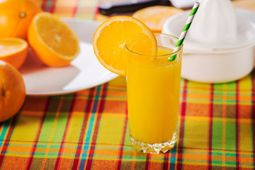 Glass of orange juice on a table with a multi-colored tablecloth, decorated with a slice of orange.