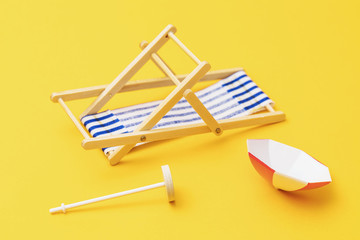 Inverted deck chair and sun umbrella on a yellow background. Spoiled vacation concept