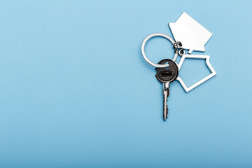 House keys with trinket on color background, top view with copy space. House key on blue background. Minimal flat lay style with place for text.