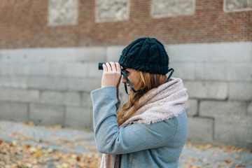 Blonde caucasian woman watches something with binoculars while on a city street