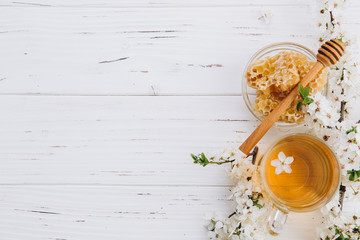 Spring composition. A cup of herbal tea and a jar of honey on a white wooden background, cherry flowers top view. Place for text. Healthy food concept.