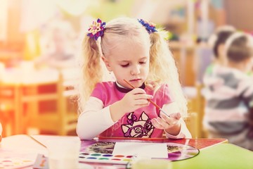 Little child with colorful paints on class background