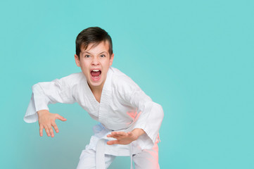 Karate young boy in white uniform makes a hit aggressively shouting o n blue background