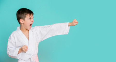 Karate young boy in white uniform makes a hit aggressively shouting o n blue background