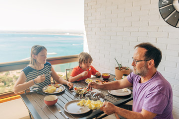 Family having lunch on the balcony with sea view, summer vacation