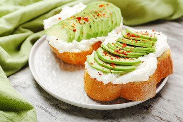 Two avocado toasts on gray plate, avocado sandwich. Fresh avocado sliced on toast of wheat bread, cream cheese.Avocado sprinkled with chili spices on gray concrete background with copy space.