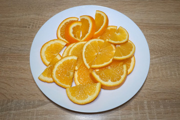 Bright slices of ripe juicy orange on a white plate on a wooden table in the kitchen