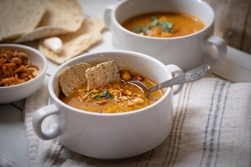 Vegan pumkin and spice soup garnished with peanuts and crackers on white wooden table