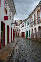 Fototapeta na wymiar Vertical urban landscape with narrow street, colorful houses and cobbled pavements in Ouro Preto city, Minas Gerais - Brazil. Ouro Preto was designed a World Heritage Site by UNESCO in 1980