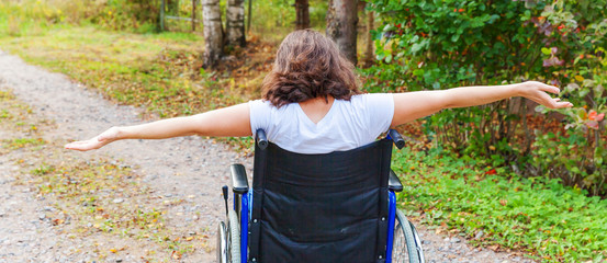 Young happy handicap woman in wheelchair on road in hospital park enjoying freedom. Paralyzed girl...